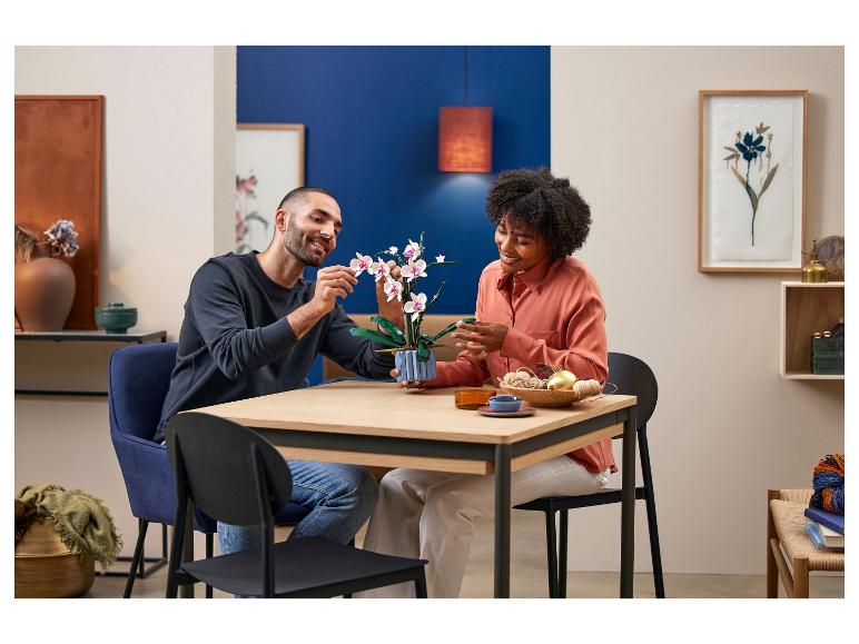 Een man en een vrouw bouwen een LEGO Orchidee set op een houten tafel.