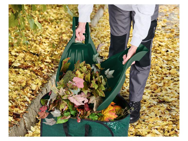 Persoon schept herfstbladeren in een groene tuinafvalzak met bladgrijpers.