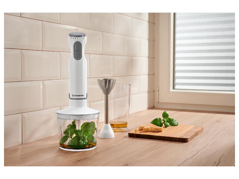 Staafmixer met hakmolen, maatbeker met olie, kaas en basilicum op snijplank.