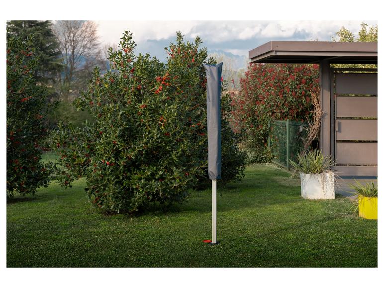 Tuinparasol in grijze hoes op gazon met struiken en een overkapping.
