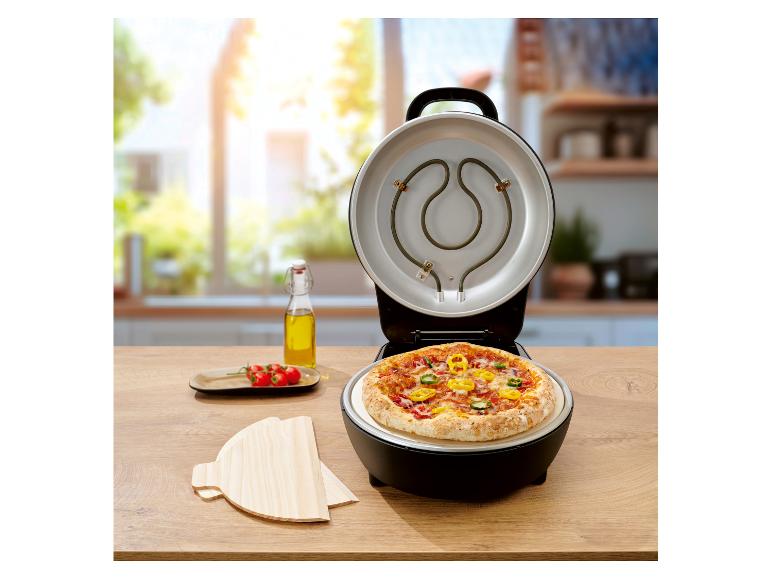 Pizzamaker met open deksel, gebakken pizza erin, olie en tomaten op een houten tafel.