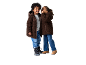 Twee kinderen in bruine teddy fleece jassen en jeans, de een fluistert de ander toe.