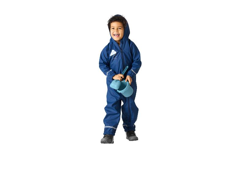 Lachende jongen in een blauw regenpak met wolkenprint, met een blauwe emmer en schep.