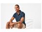 Man in marineblauwe polo en beige korte broek zittend op een witte stoel.