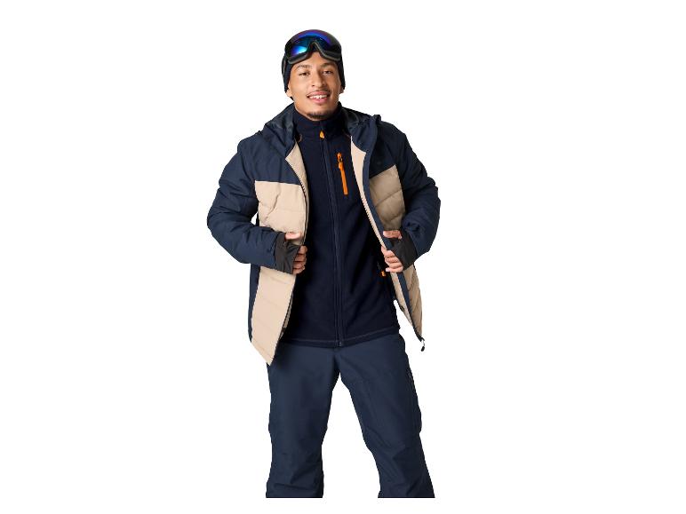 Man in donkerblauwe en beige ski-jas, broek en skibril.