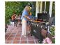 Familie barbecuet op terras, vrouw en meisje gebruiken gasbarbecue met 'GRILL MEISTER' erop.