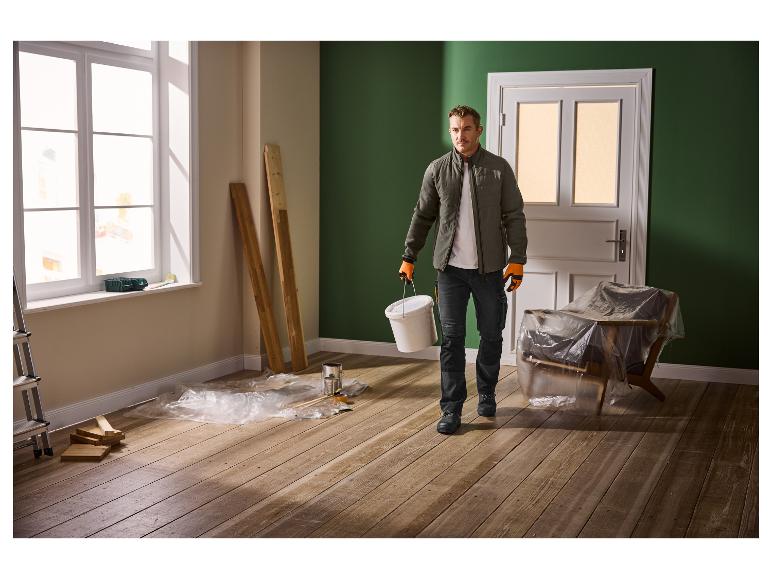 Man in werkkleding met een emmer in een kamer die wordt gerenoveerd.