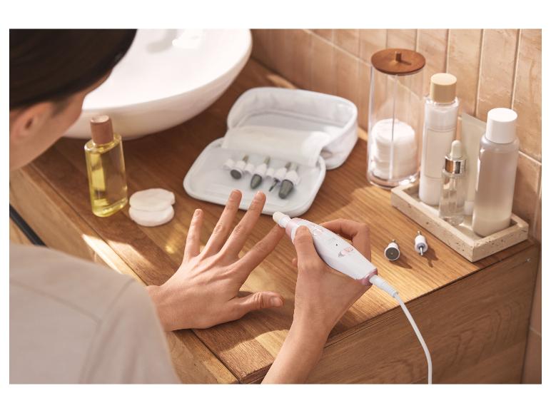 Vrouw gebruikt elektrische manicure- en pedicureset, met schoonheidsproducten in de buurt.