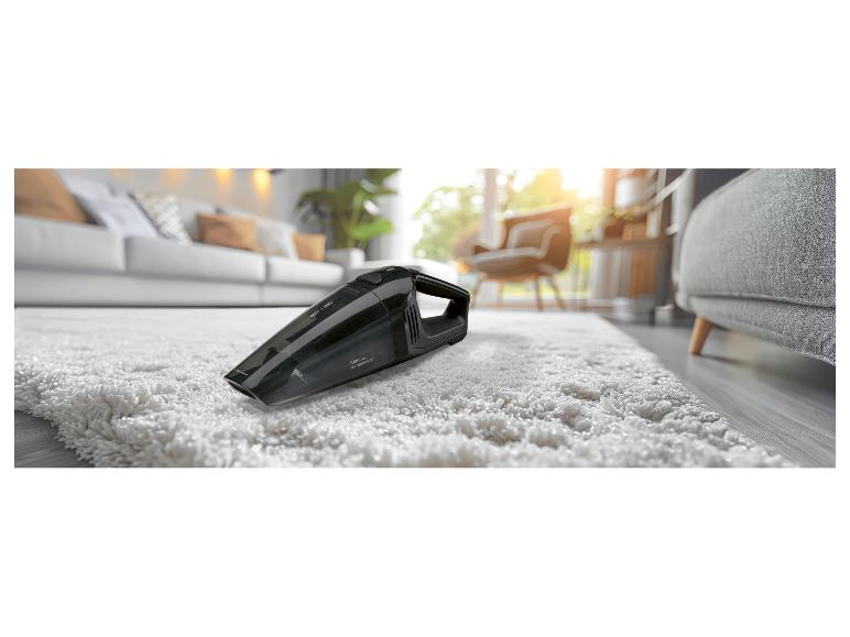 Zwarte handstofzuiger op een wit tapijt, in een lichte woonkamer.