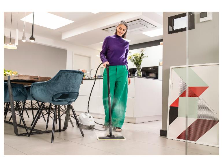 Vrouw reinigt tegelvloer in moderne woonkeuken met een stoomreiniger.