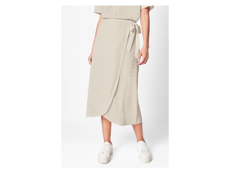 Een vrouw draagt een beige wikkelrok en witte sneakers.