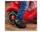 Kind in jeans en schoenen met bescherming op een rode loopauto.