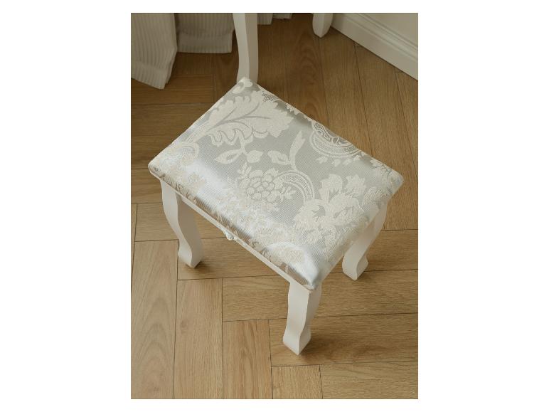 Witte kaptafelkruk met lichtgrijs bloemenpatroon op de zitting op een houten vloer.