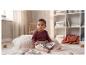 Baby in bordeauxrode romper en beige broek, zittend op een deken met een boek.