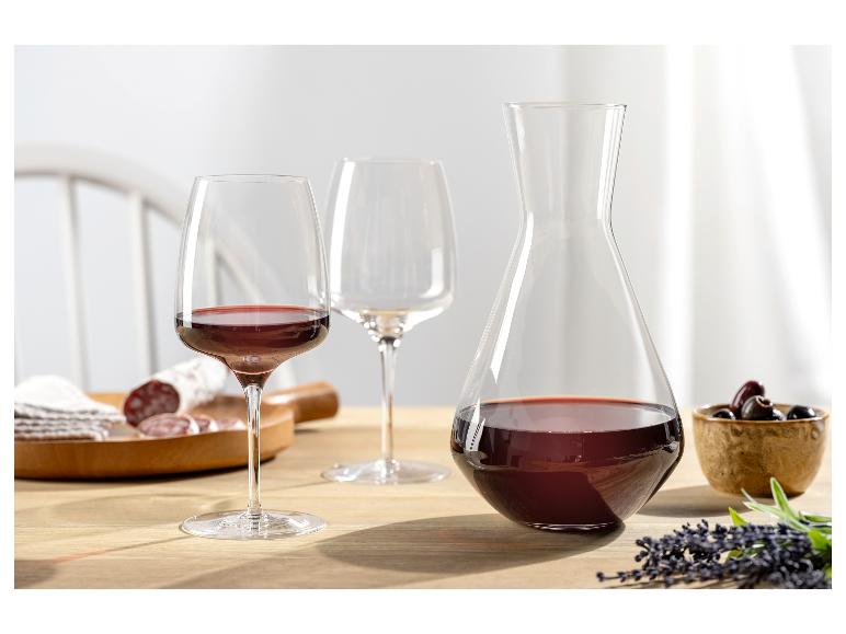 Rode wijnglas, wijnkaraf en vleeswaren op een houten tafel.