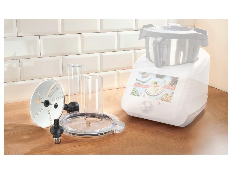 Keukenmachine met accessoires op een houten aanrecht tegen een betegelde muur.