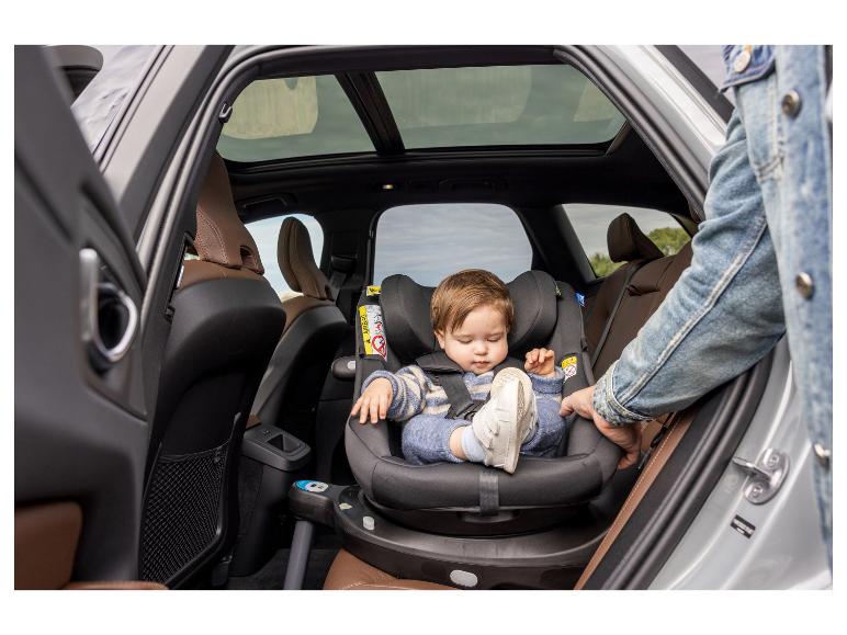 Een baby zit in een draaibare autostoel achterin een auto.