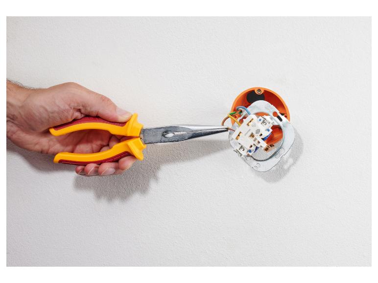 Hand met tang werkt aan een stopcontact op een witte muur.