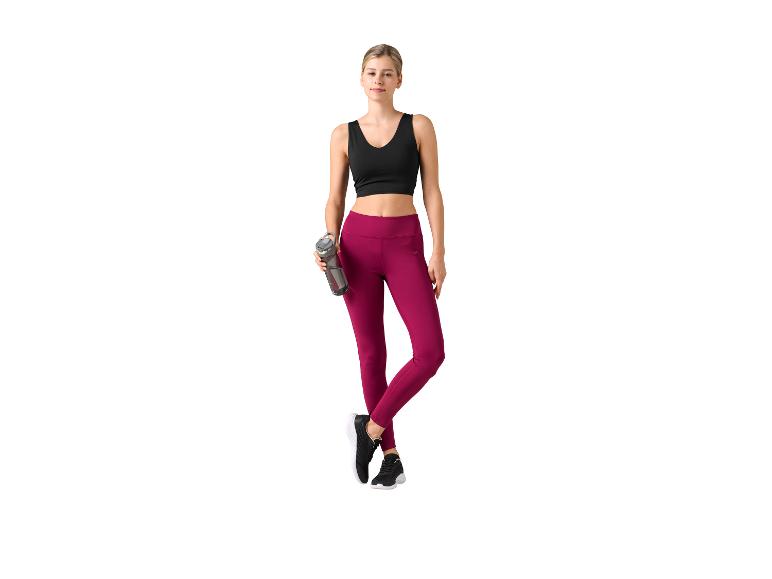 Vrouw in zwarte sportbeha en bordeauxrode legging, met waterfles.
