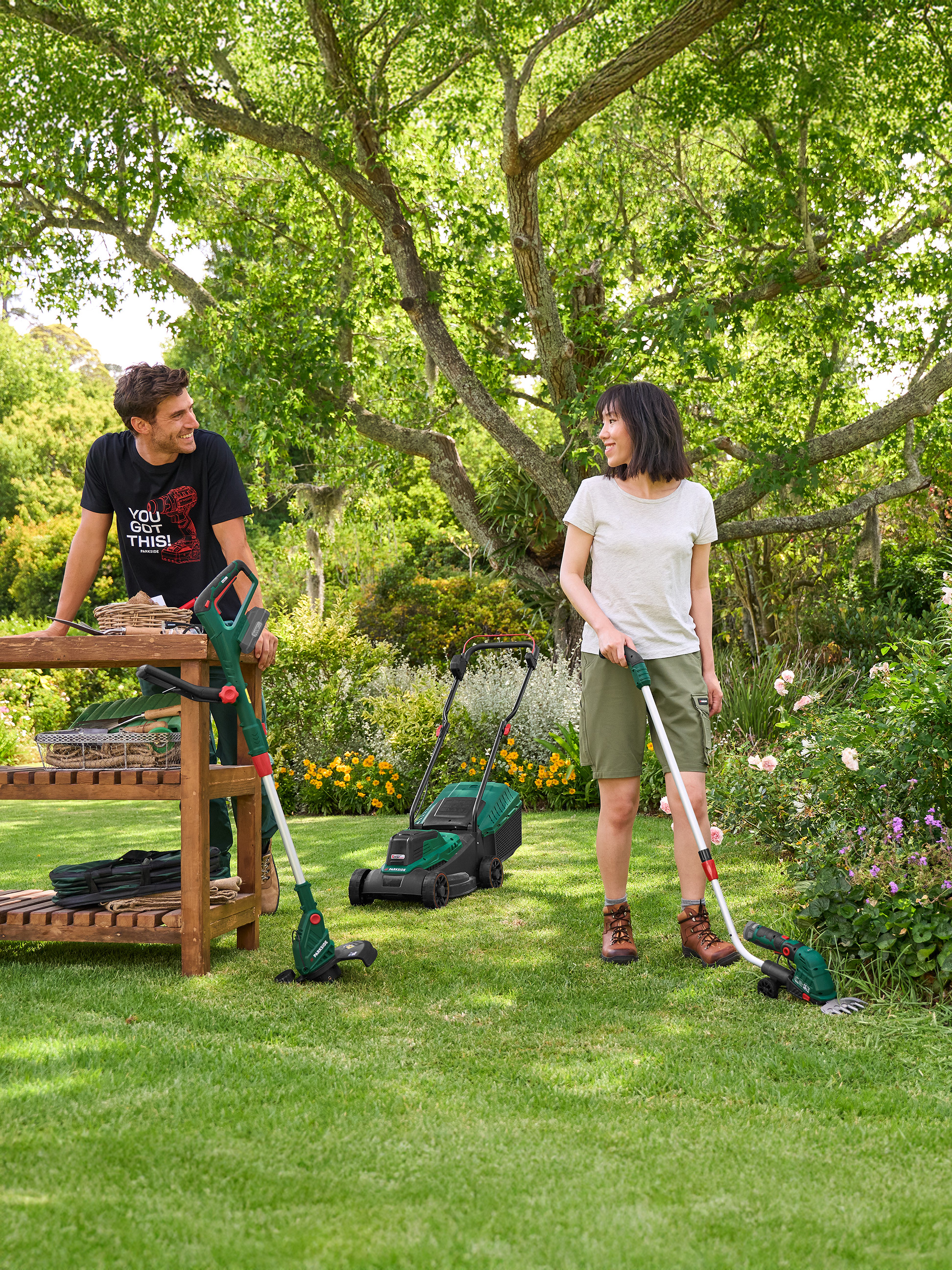 Man en vrouw in de tuin met grasmaaier, grastrimmer en grasschaar.