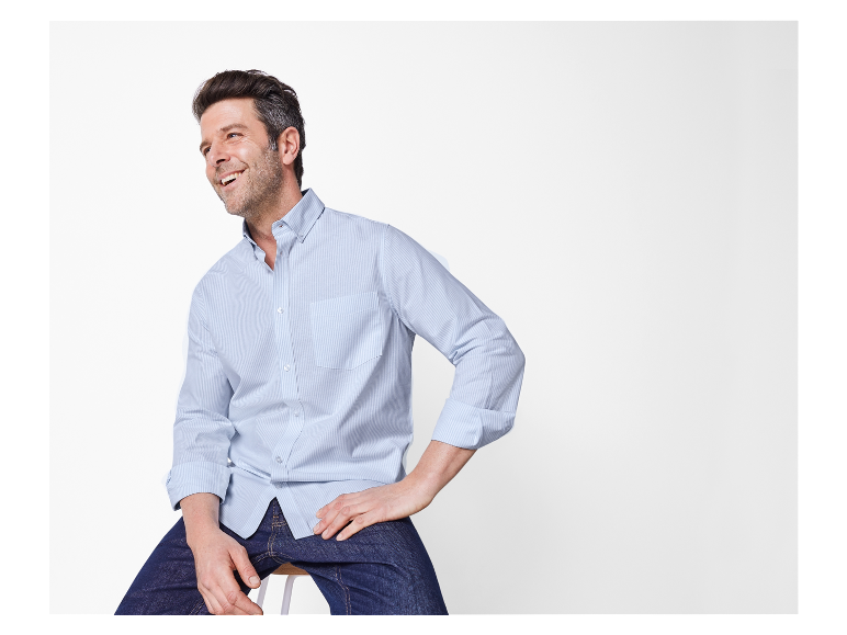 Een man lacht in een lichtblauw gestreept overhemd en jeans.