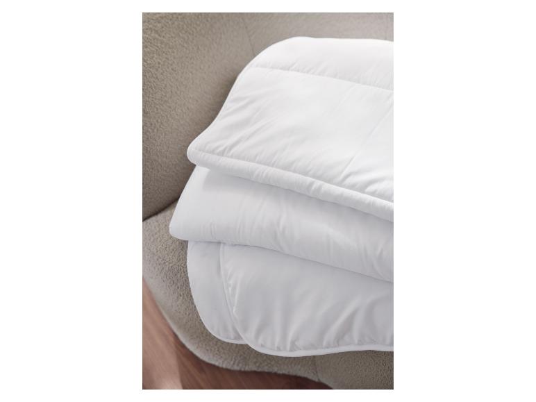 Wit opgevouwen dekbed op een beige getextureerde ondergrond.