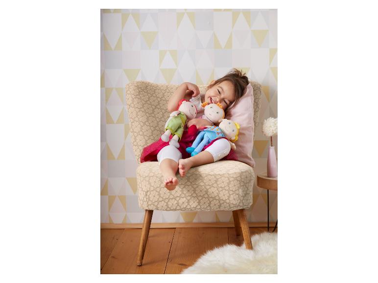 Een blij kind zit op een stoel met drie zachte poppen.