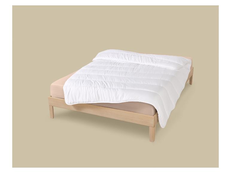 Wit dekbed op een matras met beige lakens op een houten bed.