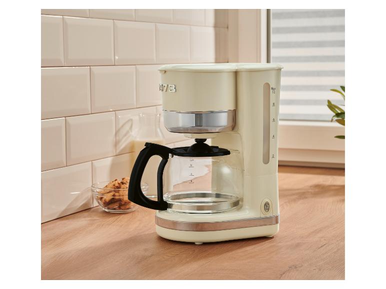 Crèmekleurig filterkoffiezetapparaat met kan, melk en koekjes op een houten aanrecht.