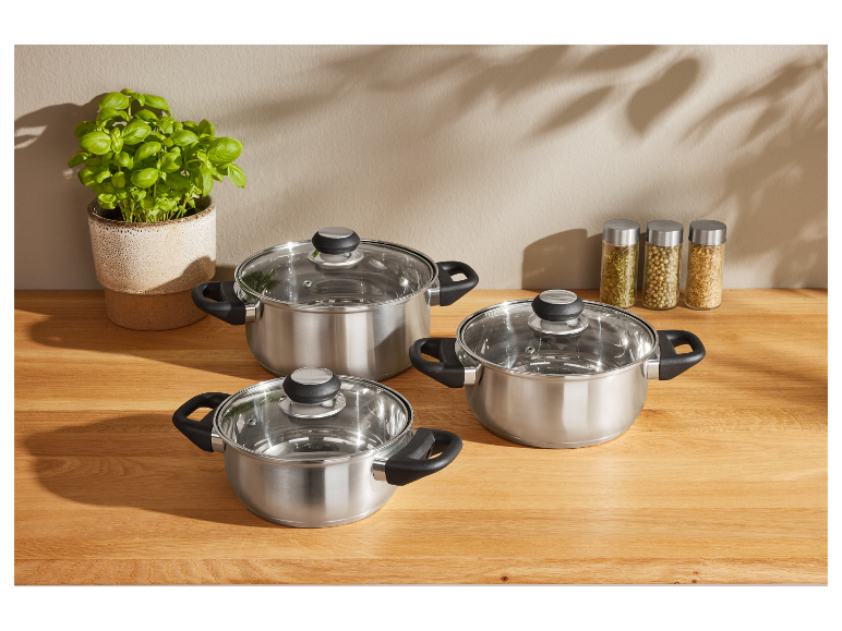 Drie roestvrijstalen pannen met glazen deksels op een houten aanrecht.