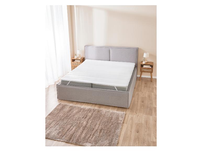 Witte matrasbeschermer op een grijs bed met houten nachtkastjes.