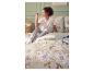 Vrouw in pyjama zittend op bed met bloemenbeddengoed, naast een nachtkastje met boeken en een mok.