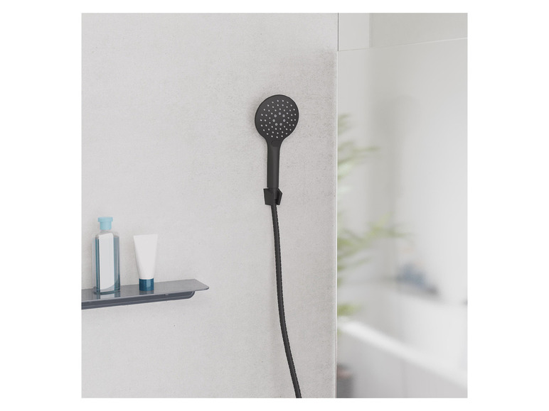 Een zwarte douchekop en een plank met toiletartikelen in een badkamer.