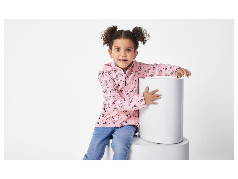 Een jong meisje zit op witte cilinders en draagt een roze ritshoodie met een schattig dierenprintje.