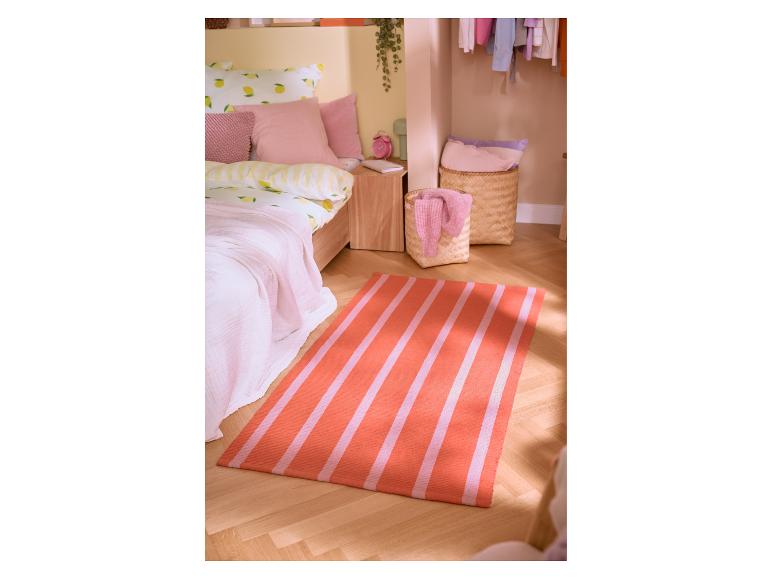 Slaapkamer met citroenprint beddengoed, roze kussens en een gestreepte oranje en roze vloerkleed.