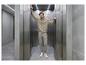 Man in grijze hoodie en joggingbroek in een moderne lift.