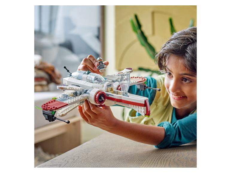 Blije jongen speelt met een wit en rood LEGO Star Wars ruimteschip en een minifiguur.