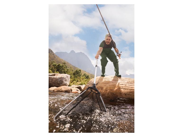 Visser in waterdicht pak met hengel en schepnet in een bergbeek.