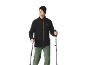 Man in zwarte fleece, groene wandelbroek en muts, met wandelstokken.
