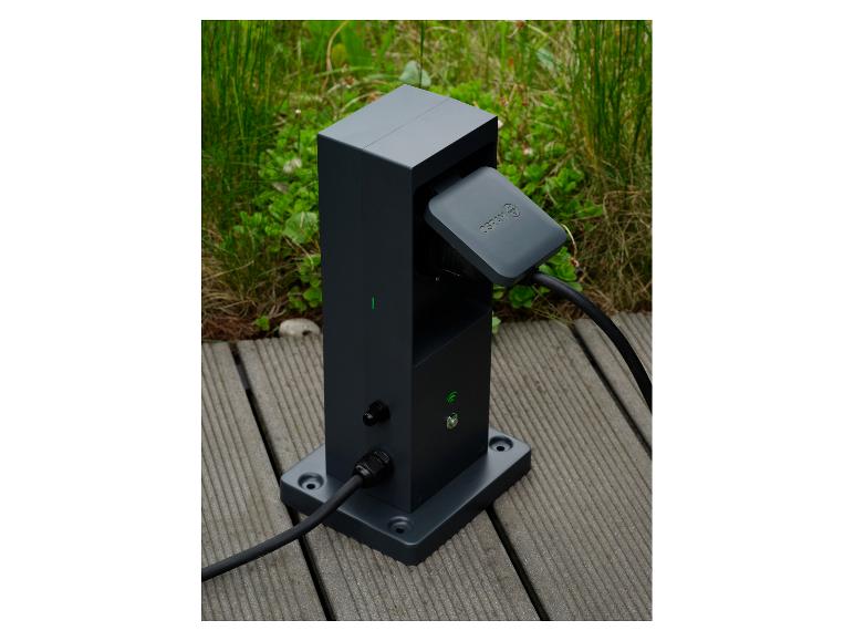 Donkergrijs laadstation voor elektrische voertuigen met aangesloten kabel op een houten vlonder.