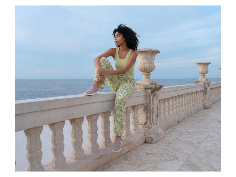 Een vrouw in een lichtgroene ESMARA® top en een broek met patroon zit op een balustrade aan zee.