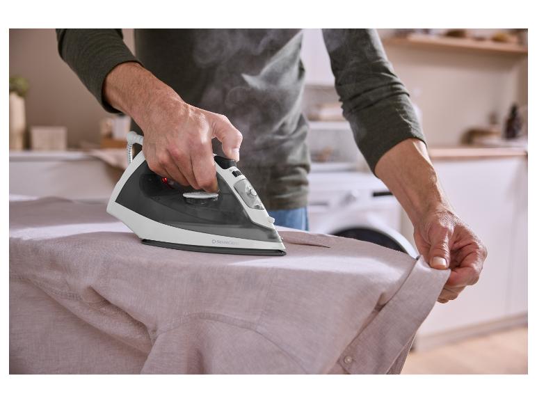 Een persoon strijkt een licht overhemd met een SilverCrest stoomstrijkijzer, stoom zichtbaar.