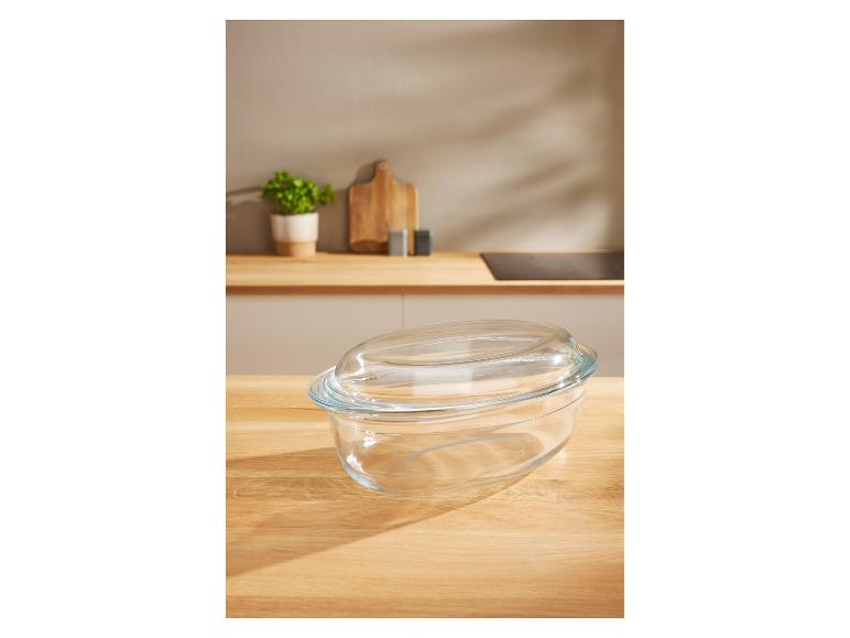 Een ovale glazen schaal met deksel op een houten oppervlak.