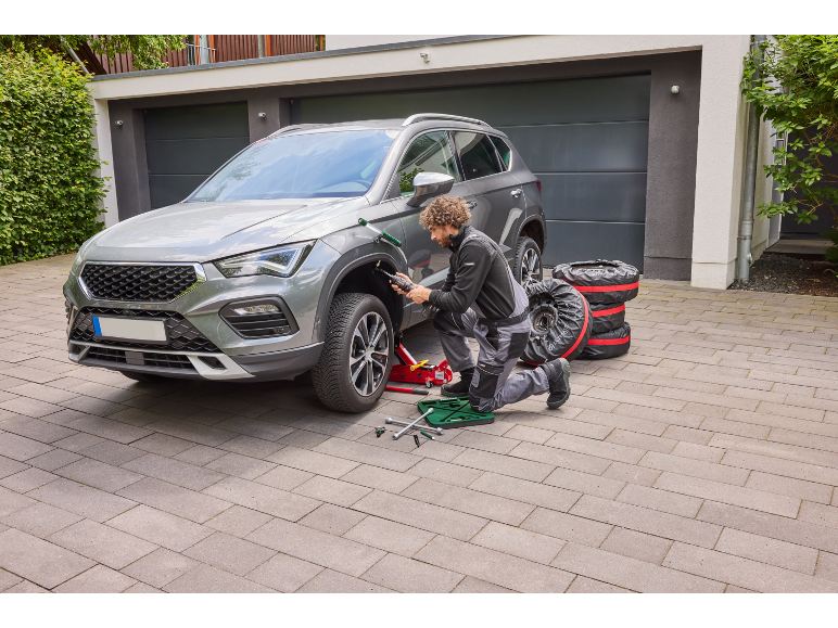 Man verwisselt autobanden, met behulp van een autokrik en een elektrische slagmoersleutel.