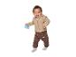 Lachende baby in een beige jasje en bruine broek met een rammelaar in de hand.
