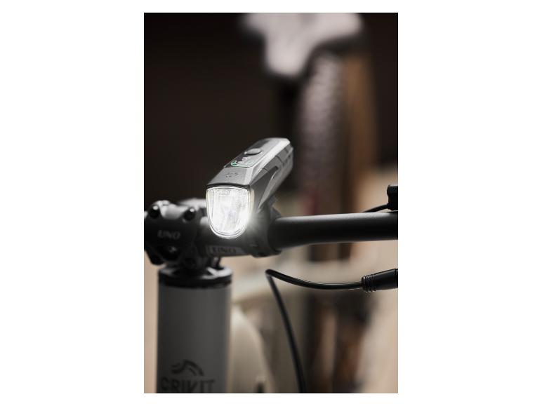 Een grijze fietslamp op een zwarte stuur van een fiets.
