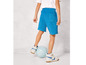 Een jongen met blauwe shorts, witte sneakers en een voetbal.