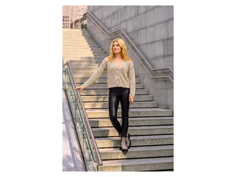Vrouw in beige vest en zwarte imitatieleer legging op betonnen trap.