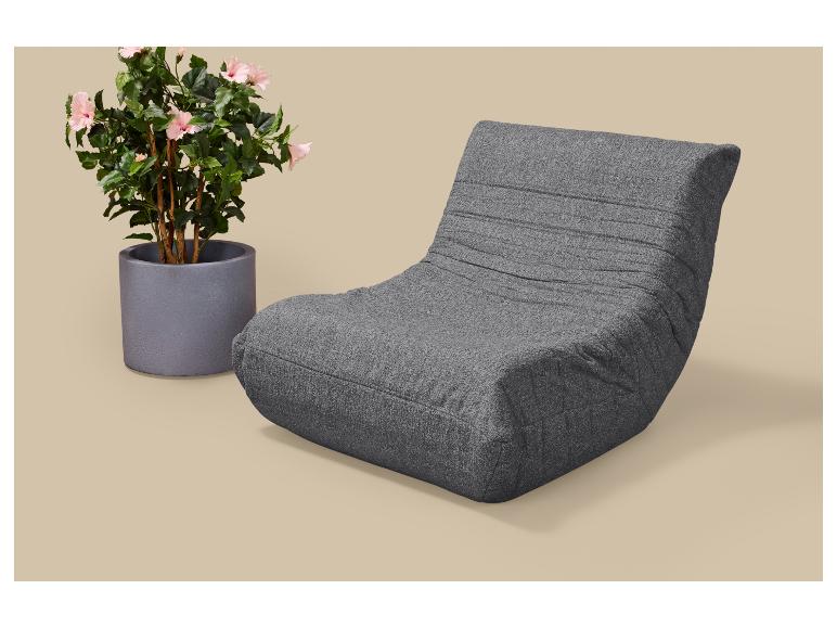 Grijze loungestoel met roze bloeiende potplant op een beige achtergrond.