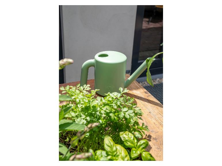 Groene gieter op een houten tafel naast verse kruiden.